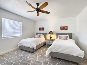 A bedroom with two beds, a ceiling fan, a nightstand with a lamp, and artwork on the walls.