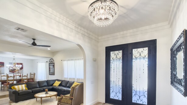 A spacious living room with a black leather sofa, a round coffee table, and a chandelier. - Gorgeous and private ranch on expansive 1.2 acres (Scottsdale)