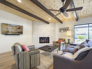 A living room with a fireplace, a ceiling fan, and a large window.