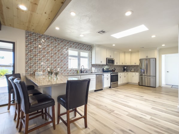 A modern kitchen with a large island, white cabinets, stainless steel appliances, and a patterned backsplash.