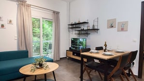 A modern living room with a sofa, a dining table with chairs, a TV, and a small plant on a side table. - Elegant Urban Escape Apt in Kolonaki (Athens)