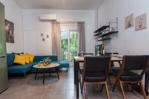 A modern living room with a blue sofa, yellow cushions, a coffee table, and a dining area with a wooden table and chairs. - Elegant Urban Escape Apt in Kolonaki (Athens)
