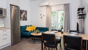 A compact kitchen with a modern refrigerator, a dining table set for two, and a sofa with yellow cushions. - Elegant Urban Escape Apt in Kolonaki (Athens)