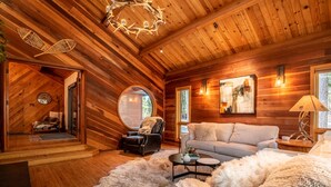 Ein gemütliches Blockhaus-Interieur mit Holzboden, einem runden Spiegel, einer Couch, einem Couchtisch und einem flauschigen Teppich.