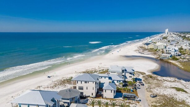 Una vista aerea di una zona costiera con proprietà sulla spiaggia, tra cui case e un albergo con un cartello che riporta la scritta "The Seaside Inn".
