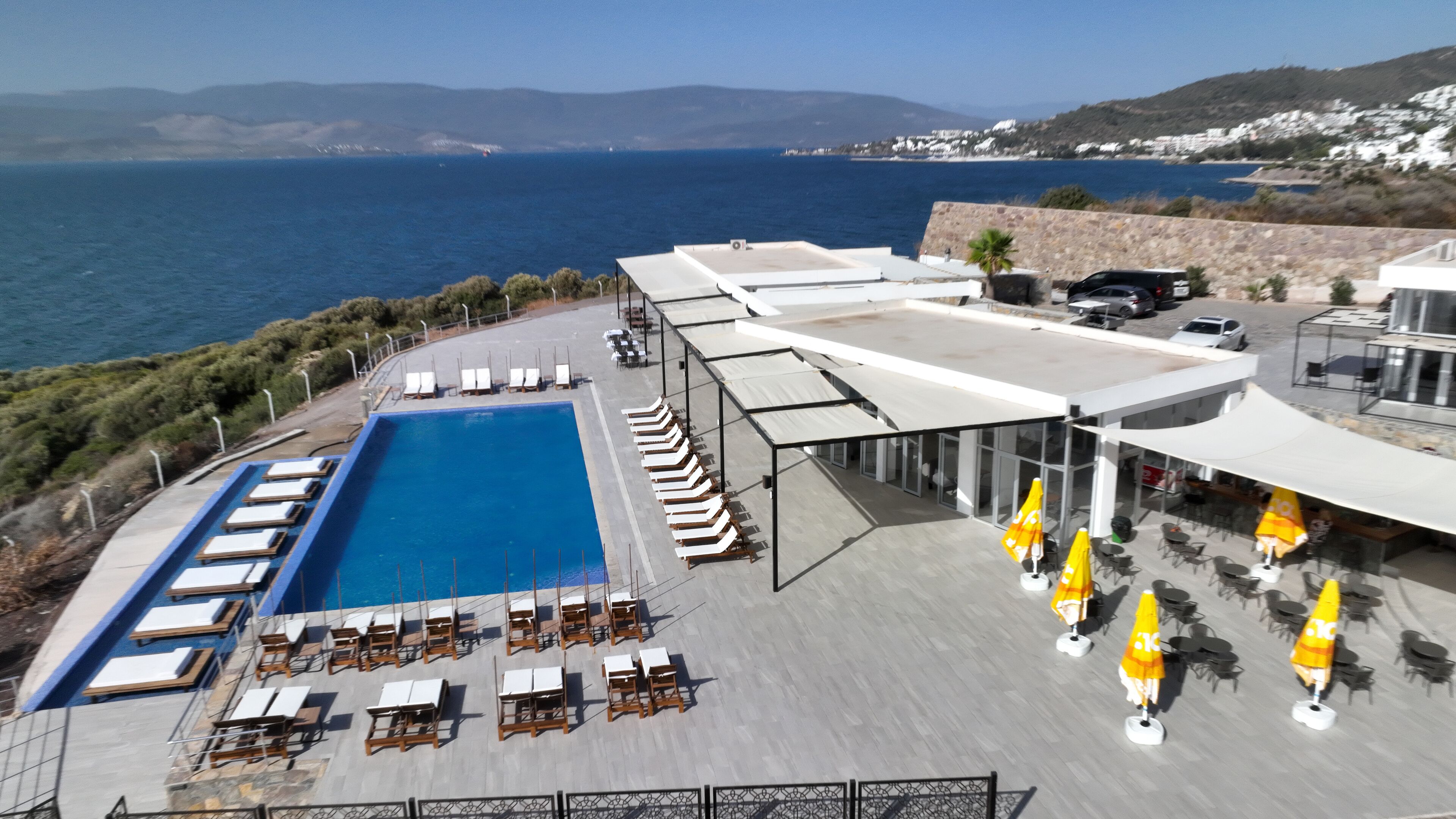 A rooftop pool area with lounge chairs and umbrellas, overlooking a coastal landscape.
