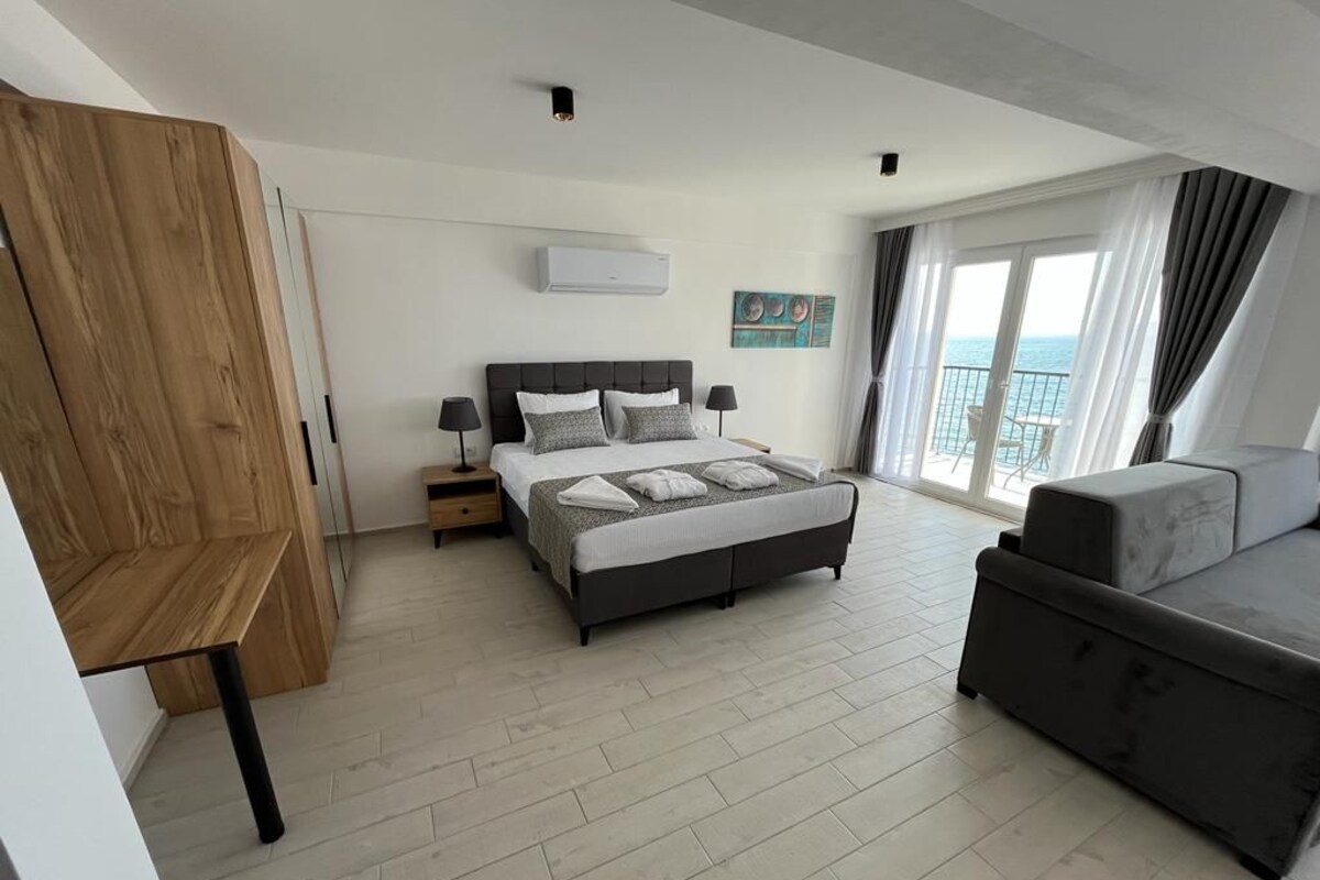 A modern hotel room with a bed, a sofa, a wooden desk, and a large window with a view.
