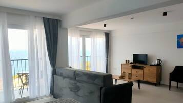 Una sala de estar moderna con un sofá gris, un mueble de televisión de madera y un balcón con vista al mar.