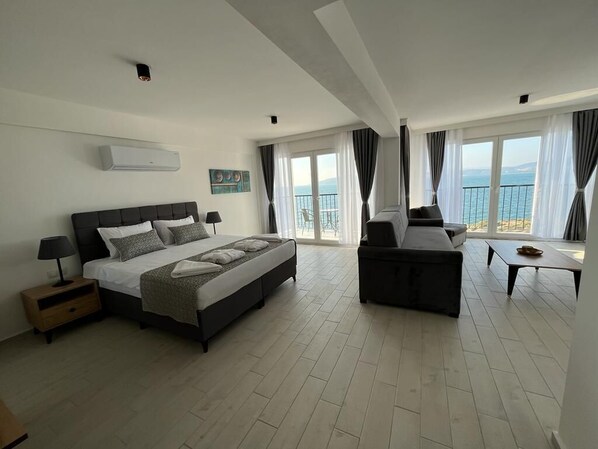 A modern hotel room with a large bed, a sofa, a small table, and a balcony with a view of the sea. - Ni Marin Hotel (Milas)