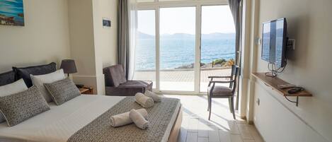 Habitación de hotel con una cama grande, televisión, sillón y vista al mar.