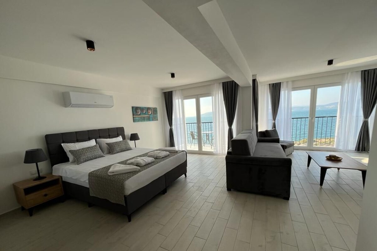 Habitación de hotel moderna con una cama grande, un sofá, una mesita y un balcón con vista al mar.