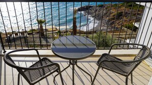 A balcony with a round table and two wicker chairs, overlooking a rocky coastline and the sea. - Ni Marin Hotel (Milas)