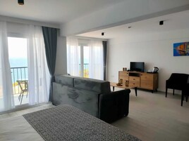 Una sala de estar moderna con un sofá gris, un mueble bajo para la televisión de madera y un balcón con vistas al mar.