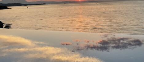 A sunset over a calm sea with distant mountains and a pier.