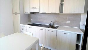 A modern kitchen with white cabinets, a black stove, and a white dining table with chairs. - Affittimoderni La Maddalena - MADA28 (La Maddalena)