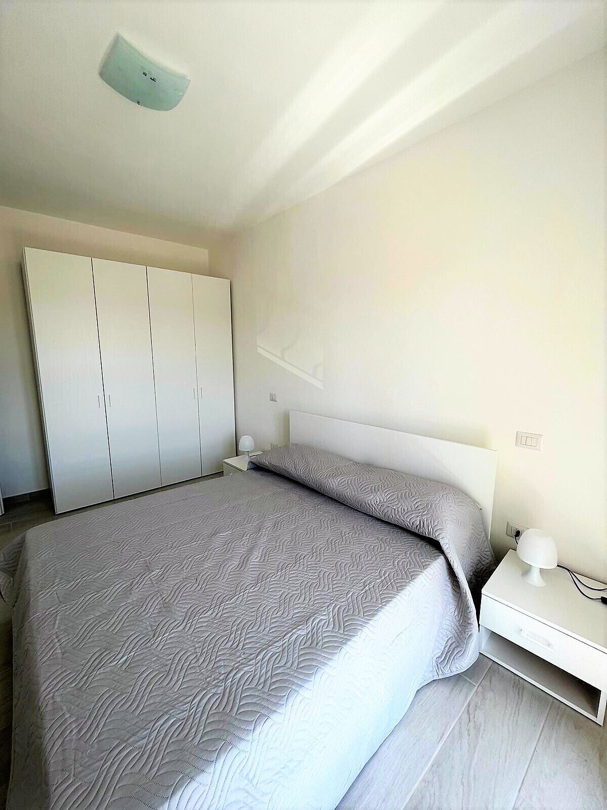 A modern bedroom with a bed, a wardrobe, a nightstand, and a ceiling light fixture.