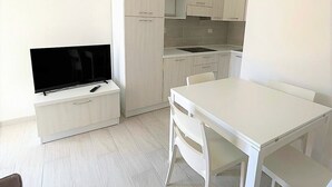 Eine moderne Küche mit weißen Schränken, einem Esstisch und einem Flachbildfernseher.