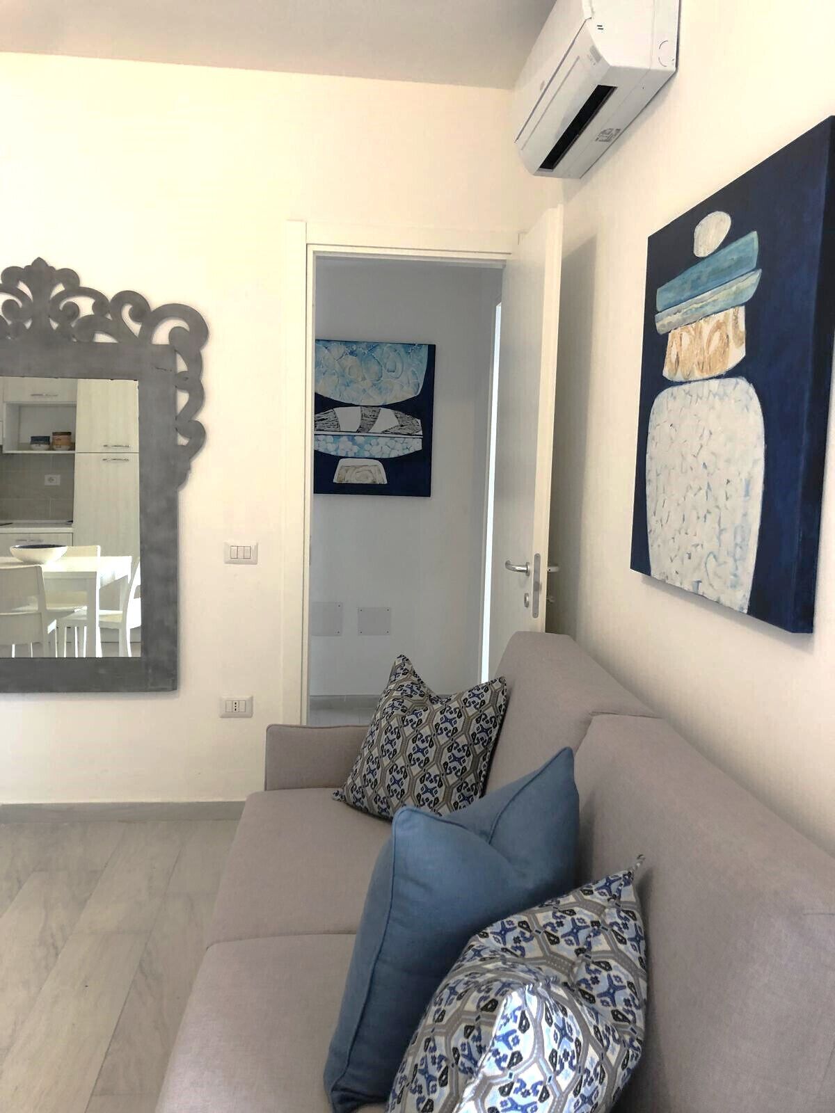 A living room with a beige sofa, patterned pillows, a large mirror, and abstract wall art.
