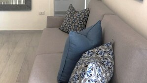 Ein Wohnzimmer mit einem beigefarbenen Sofa, gemusterten Kissen, einem großen Spiegel und abstrakter Wandkunst.