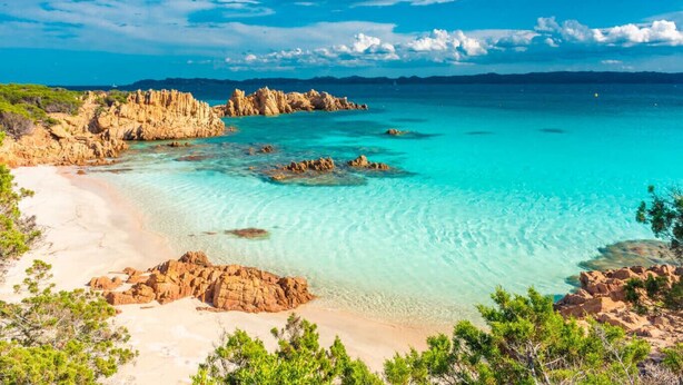 Eine Küstenlandschaft mit klarem türkisblauem Wasser, Felsformationen und einem Sandstrand.