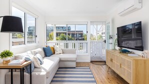 A modern living room with a sofa, TV, and a view of buildings through large windows.