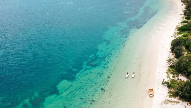 An aerial view of a beach with clear turquoise waters, a sandy shore, and some vegetation on the right. - Shoal Bay Beach House- Three (Shoal Bay)