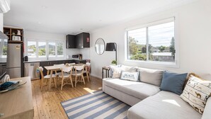 A modern kitchen with a dining area, a sofa with a view, and a large window.