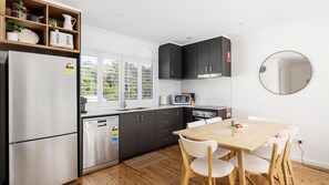Cocina moderna equipada con refrigerador, microondas, estufa y lavavajillas. Hay una mesa de comedor con sillas y una ventana con persianas.