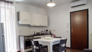 Een compacte keuken met witte kastjes, een eettafel met vier stoelen, een koelkast en een oven.