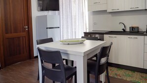 Een kleine keuken met een eettafel, stoelen, een televisie en een koelkast.