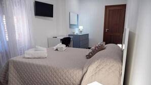 Een hotelkamer met een bed, een bureau, een stoel, een dressoir, een televisie en een deur.