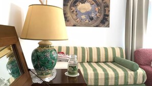 Una habitación acogedora con un sofá a rayas, un jarrón verde, una lámpara y un cuadro en la pared.