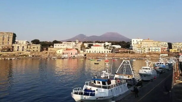 Un muelle con barcos amarrados, edificios al fondo y una montaña en la lejanía.