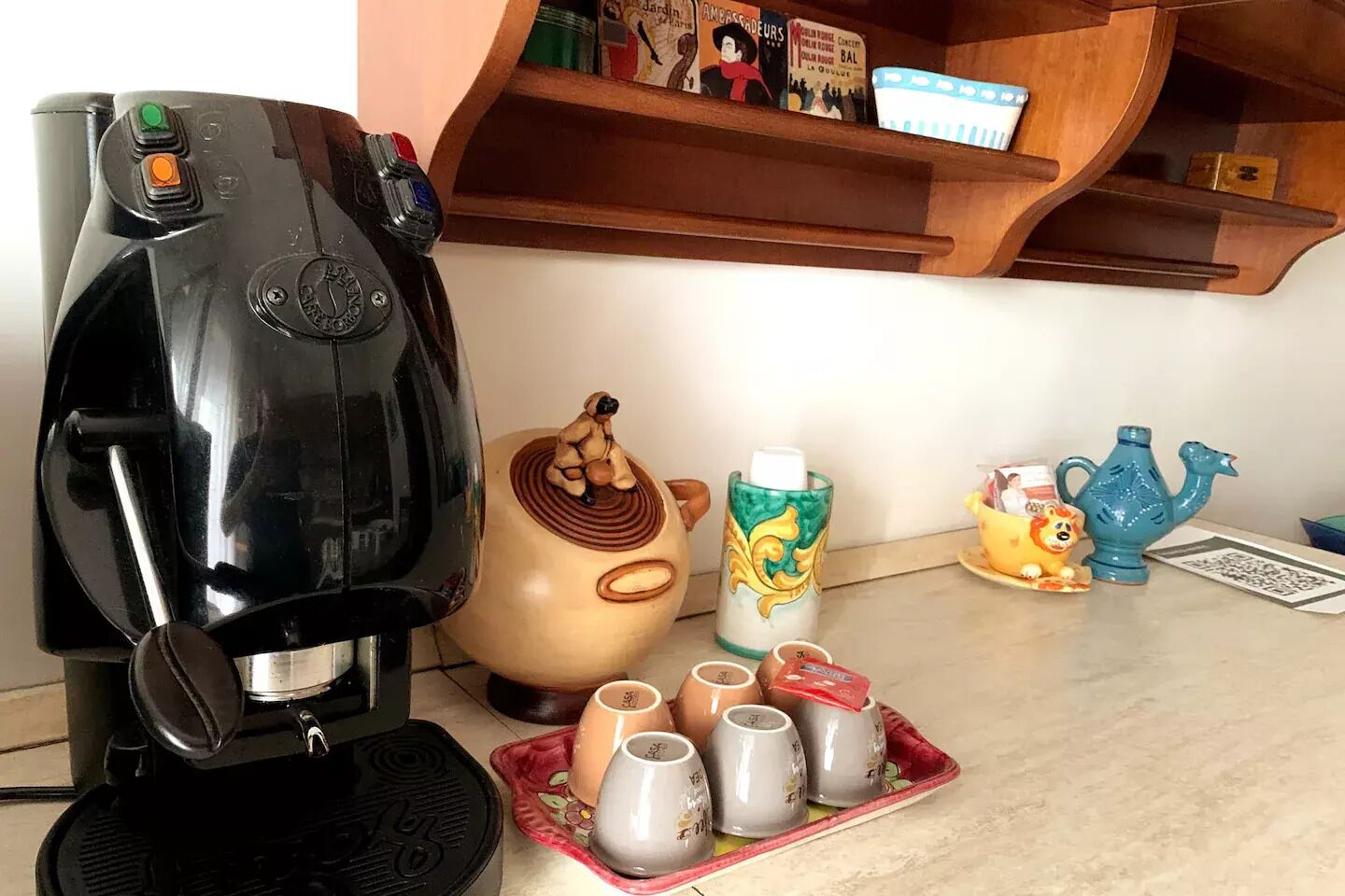 A kitchen counter with a coffee maker, a decorative pig-shaped container, a colorful mug, a teapot, and a tray with cups.