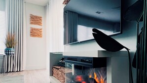 A modern living room with a fireplace, a flat-screen TV mounted above it, and a potted plant. - Home away from Home. Fresh, Bright Condo just steps away from the beach (Hilton Head Island)