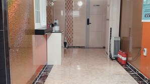 Hotellin aula, jossa on vastaanottotiski, kuvioidut seinät, kattokruunu ja palosammutin.