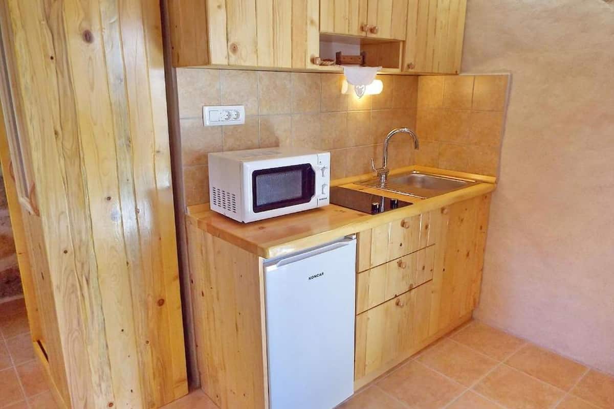 A compact kitchen with wooden cabinets, a microwave, a sink, and a small refrigerator.