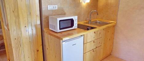 Une cuisine compacte avec des meubles en bois, un four à micro-ondes, un évier et un petit réfrigérateur.