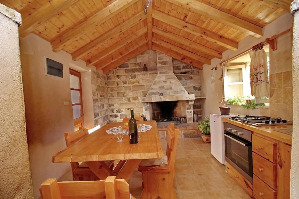 A rustic kitchen with a stone fireplace, wooden ceiling, and a dining table with chairs.