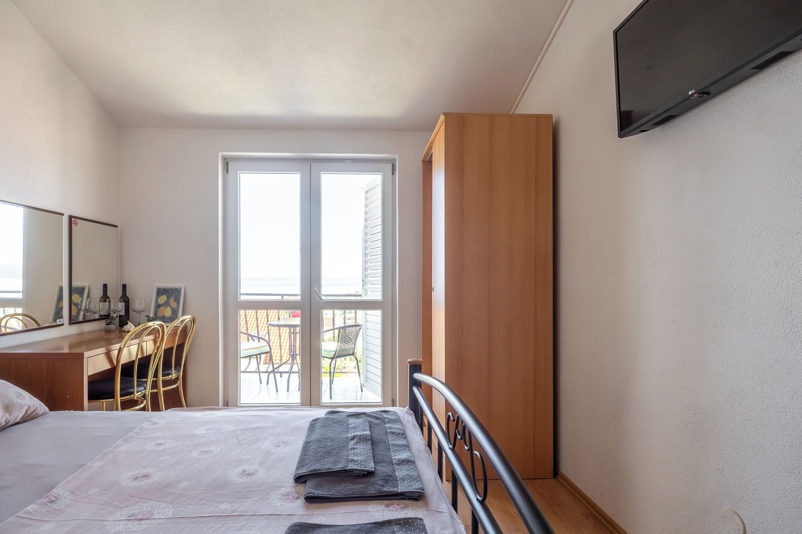 A bedroom with a bed, a desk, a chair, a wardrobe, and a TV.