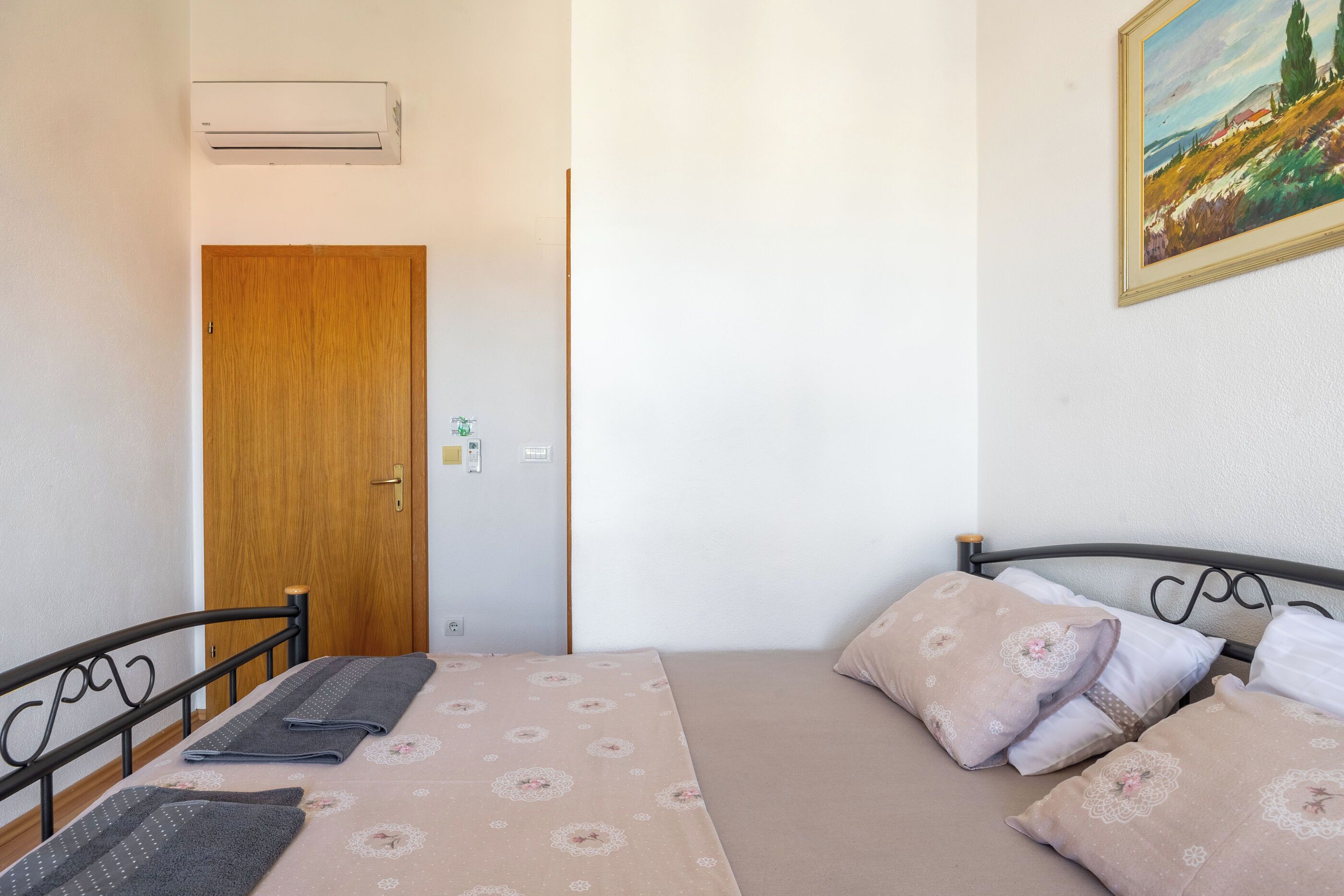 A bedroom with a bed, pillows, a wooden door, and an air conditioning unit.