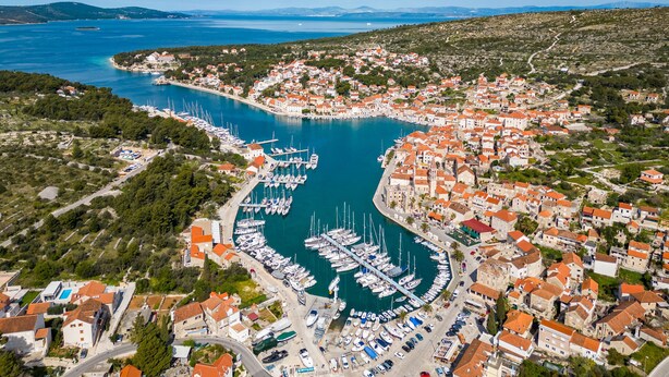 An aerial view of a coastal town with a marina filled with boats, surrounded by residential buildings with red roofs. - Apartment Magical View (Milna)