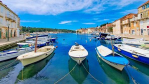 A marina with boats docked, buildings along the waterfront, and a clear blue sky. - Apartment Magical View (Milna)