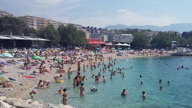 A crowded beach with people swimming and sunbathing, umbrellas, and beach chairs. - Apartment Zeljana (Split)