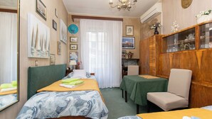 A hotel room with two beds, a dining table, a chair, and a cabinet with decorative items. - Apartment Zeljana (Split)