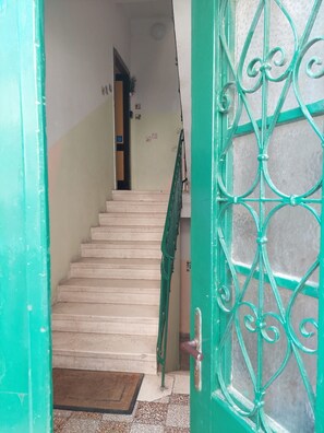 A staircase leading to an upper floor, a green door with a metal gate, and a small mat at the entrance. - Apartment Zeljana (Split)