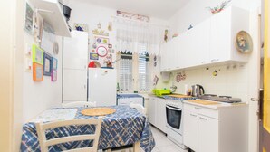 A compact kitchen with white cabinets, a stove, and a dining area with a table and chairs. - Apartment Zeljana (Split)