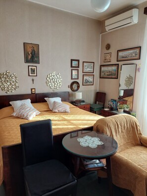 A hotel room with a bed, a round table with a lace doily, a chair, a small table with a lamp, and various framed pictures on the walls. - Apartment Zeljana (Split)