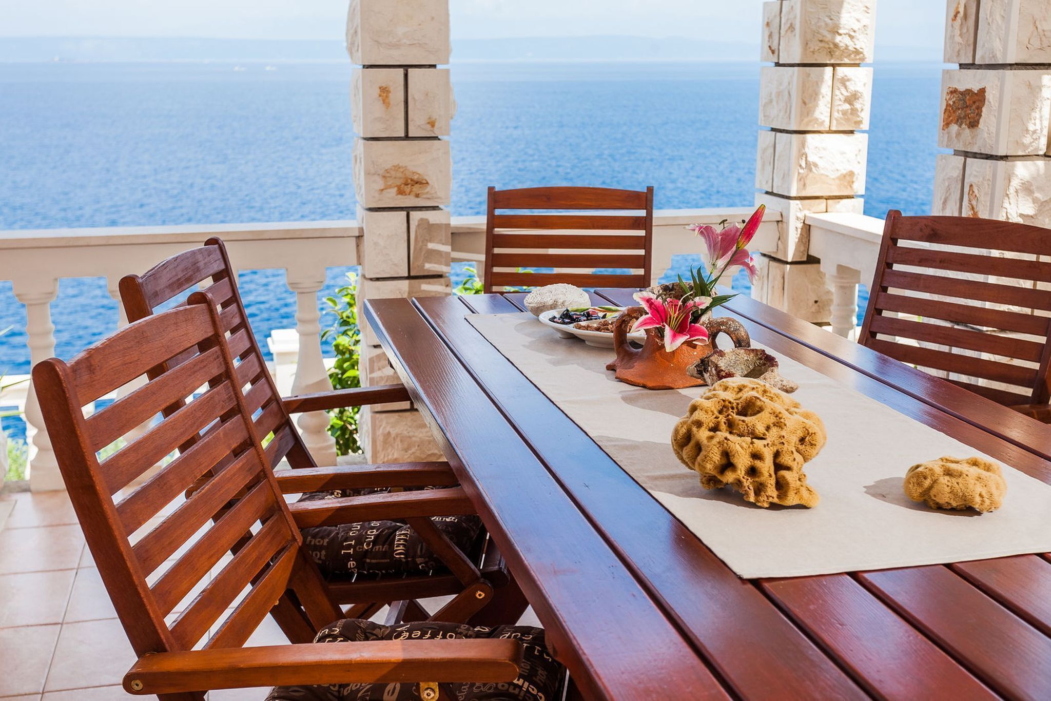 Ein Holztisch gedeckt mit Speisen, einer Blumenvase und Blick aufs Meer.