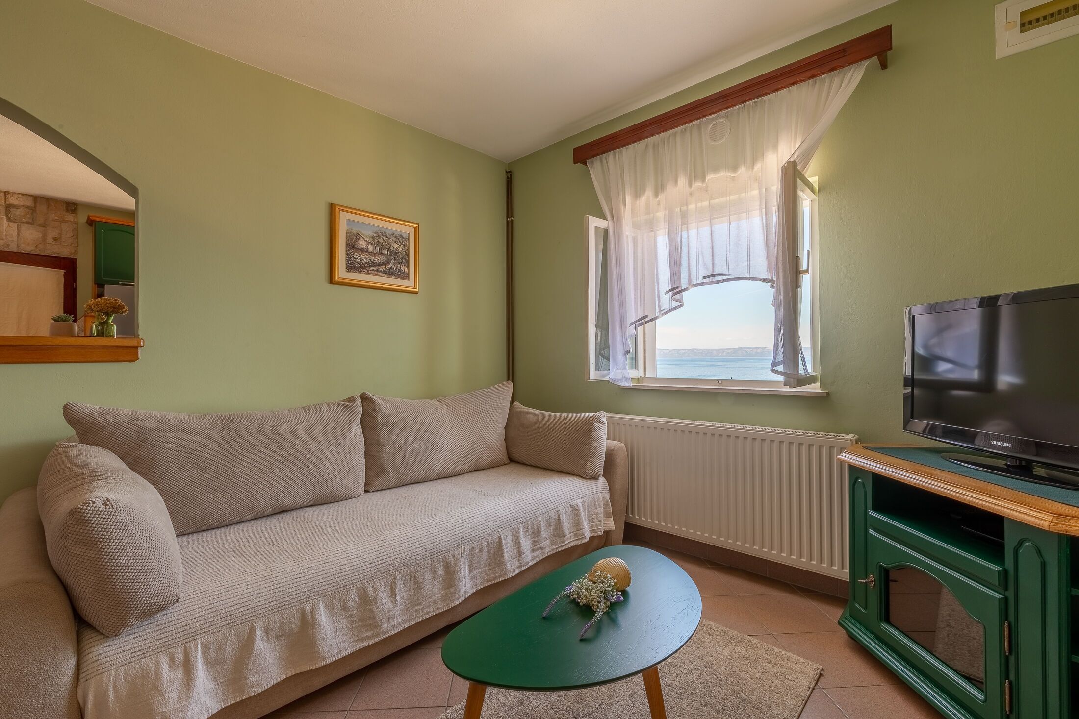 Una sala de estar con un sofá, una mesita con un objeto decorativo, un televisor sobre un mueble de madera y una ventana con vistas.